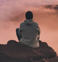 A sole person sitting at the top of a mountain over looking a sky filled with pink clouds.